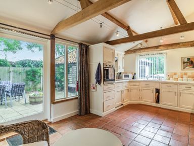 A kitchen with wooden beams on the ceiling and white cabinets next to a patio door at Ducksfoot Barn Bush Green near Pulham Market