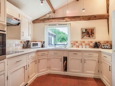 A kitchen with white cabinets microwave and toaster near a window with vertical blinds at Ducksfoot Barn in Bush Green near Pulham Market