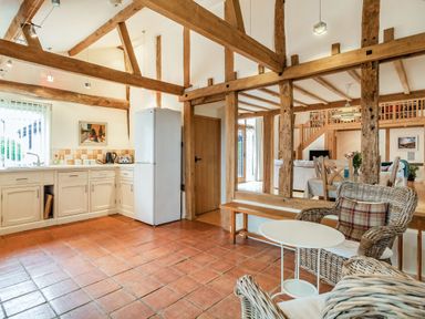 A kitchen and dining area with wooden beams terracotta floor and wicker chairs at Ducksfoot Barn in Bush Green near Pulham Market