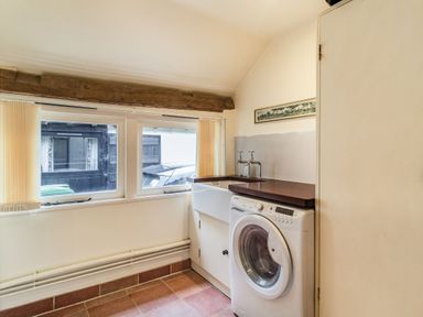 A laundry room with a washing machine a sink windows and wooden countertop at Ducksfoot Barn in Bush Green near Pulham Market