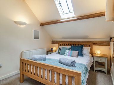 A bedroom with a wooden bed and pillows under a skylight at Ducksfoot Barn in Bush Green near Pulham Market