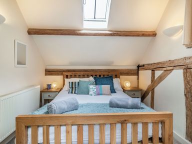 A bedroom with a wooden bed frame and bedding with cushions and towels at Ducksfoot Barn Bush Green near Pulham Market