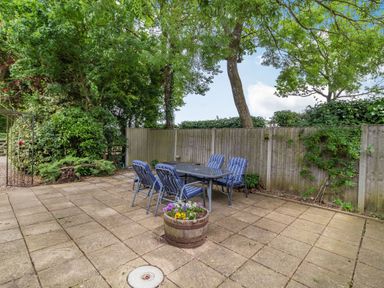 An outdoor patio with a table and six chairs surrounded by trees and a wooden fence at Ducksfoot Barn in Bush Green near Pulham Market