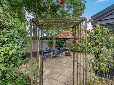 A patio with a metal pergola and outdoor dining set surrounded by plants at Ducksfoot Barn Bush Green near Pulham Market