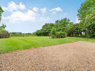 A gravel area next to a grassy lawn and trees at Ducksfoot Barn Bush Green near Pulham Market