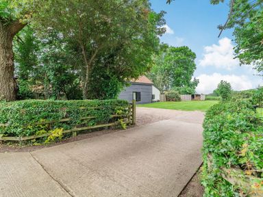 A driveway leading to a black wooden building with a tiled roof surrounded by trees and hedges at Ducksfoot Barn Bush Green near Pulham Market
