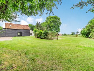 A grassy yard with trees a wooden shed and a black and brown building at Ducksfoot Barn Bush Green near Pulham Market