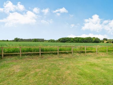 A grassy field with a wooden fence and trees under a partly cloudy sky at Ducksfoot Barn in Bush Green near Pulham Market