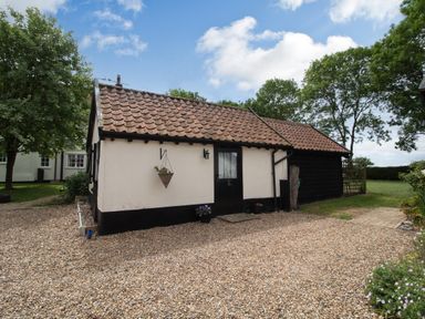 A single-story cottage with tiled roof gravel driveway and surrounding trees at Garden Cottage in Bush Green near Pulham Market