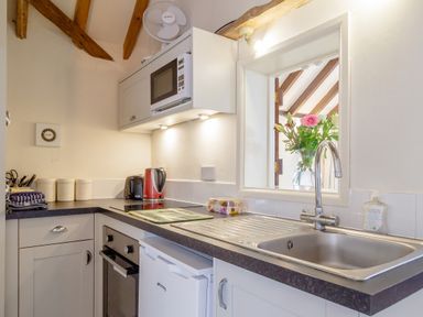 A kitchen with a sink, microwave, kettle, toaster, and flowers near the window at Garden Cottage Bush Green near Pulham Market