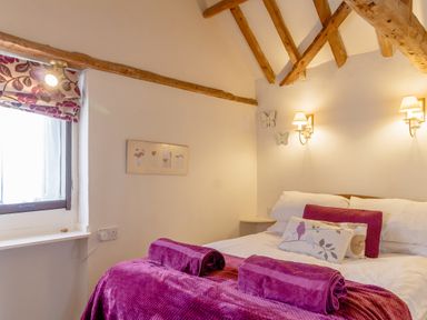 A bedroom with a bed covered in purple throws and pillows under wooden ceiling beams at Garden Cottage in Bush Green near Pulham Market