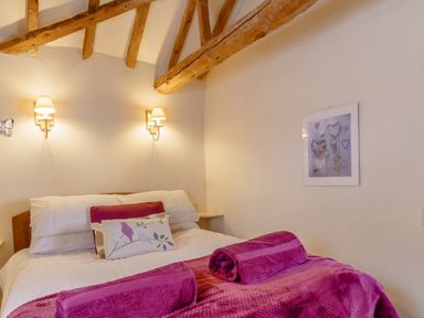 A bedroom with a bed white pillows rolled towels and exposed wooden beams at Garden Cottage Bush Green near Pulham Market