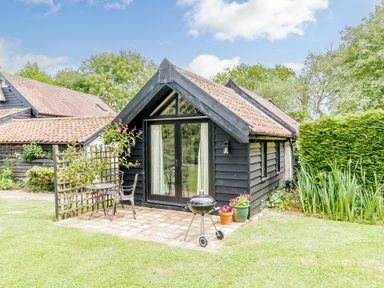 A small black wooden cottage with a tiled roof and patio furniture in a garden at Garden Cottage in Bush Green near Pulham Market