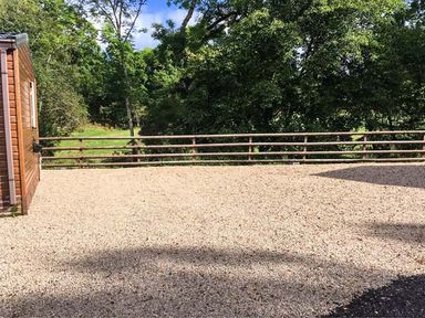 A gravel area with a wooden fence and trees in the background at The Four Oaks Chalet in Blaich near Fort William