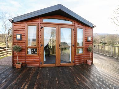 A wooden cabin with glass doors and windows on a wooden deck with potted plants at The Four Oaks Chalet in Blaich near Fort William