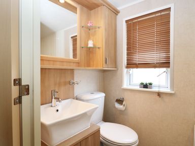 A bathroom with a sink a toilet a window with wooden blinds and wooden cabinets at The Four Oaks Chalet in Blaich near Fort William