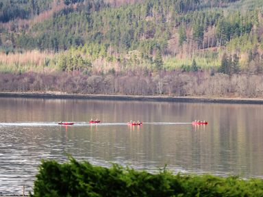 A lake with four red canoes and people paddling surrounded by forest and hills at The Four Oaks Chalet in Blaich near Fort William