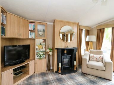 A living room with a television unit a fireplace with a round mirror and an armchair at The Four Oaks Chalet in Blaich near Fort William