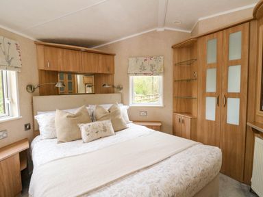 A bedroom with a double bed two windows wooden cupboards and bedside tables at The Four Oaks Chalet in Blaich near Fort William