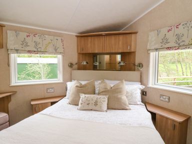A bedroom with a bed between two windows and wooden cabinets above the bed at The Four Oaks Chalet in Blaich near Fort William