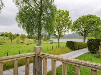 A wooden fence overlooks a gravel path with trees and a lake in the background at The Four Oaks Chalet in Blaich near Fort William