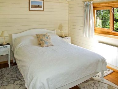 A bedroom with a white bed and floral pillows next to two bedside tables with lamps by a window at Cropvale Lodge in Cropthorne near Pershore