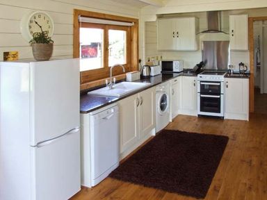 A kitchen with white cabinets appliances a brown rug and a window with wooden frame at Cropvale Lodge in Cropthorne near Pershore