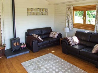 A sitting room with two black leather sofas a wood burning stove and a window with curtains at Cropvale Lodge Cropthorne near Pershore