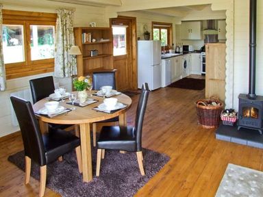 A dining area with a round table set for four next to a kitchen with white appliances and wooden floors at Cropvale Lodge in Cropthorne near Pershore