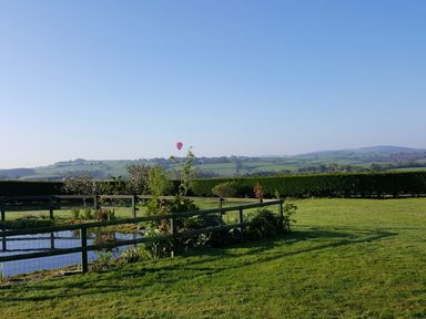 A garden with a small pond grass and fence with rolling hills in the background at The Old Granary in Polyphant near Launceston