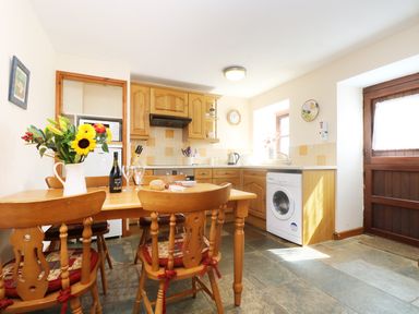 A kitchen with wooden cabinets wooden dining table with chairs and a washing machine near a wooden door at The Old Granary Polyphant near Launceston