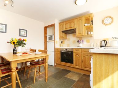 A kitchen with wooden cabinets a dining table with flowers and chairs at The Old Granary in Polyphant near Launceston