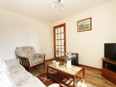 A living room with armchairs a coffee table with flower vase a television and a framed picture on the wall at The Old Granary in Polyphant near Launceston