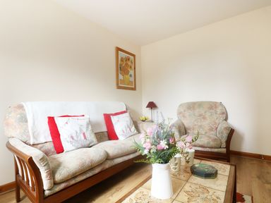 A living room with floral sofas a coffee table with flowers and cups and a painting on the wall at The Old Granary in Polyphant near Launceston