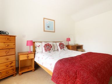 A bedroom with a double bed red floral bedding two wooden bedside tables with pink lamps a wooden chest of drawers and a wooden dressing table at The Old Granary in Polyphant near Launceston