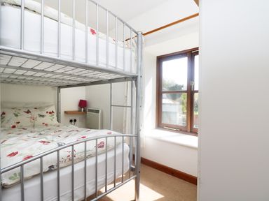 A bedroom with a metal bunk bed floral bedding a window and a small wall shelf with a lamp at The Old Granary in Polyphant near Launceston