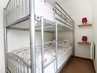 A bedroom with a metal bunk bed and a wall with two shelves holding table lamps at The Old Granary in Polyphant near Launceston