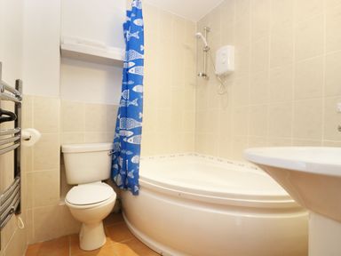 A bathroom with a corner bathtub toilet sink and blue shower curtain with fish pattern at The Old Granary in Polyphant near Launceston