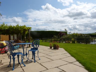 A patio with blue metal table and chairs next to a garden and pond at The Old Granary in Polyphant near Launceston
