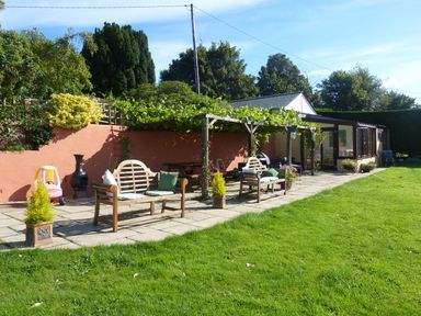 An outdoor patio with benches, a pergola with plants, a small play car, and a grassy lawn at The Old Granary in Polyphant near Launceston