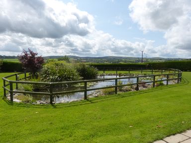A pond surrounded by a wooden fence with plants and grass in a rural landscape at The Old Granary in Polyphant near Launceston