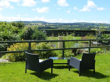 A garden with two black chairs and a glass table overlooking plants and countryside hills at The Old Granary in Polyphant near Launceston