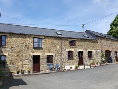 Stone buildings with brown doors and windows with blue chairs and flower pots outside at The Old Granary Polyphant near Launceston