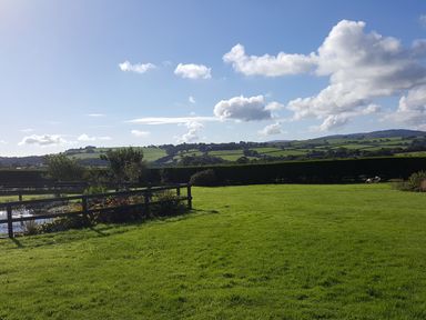 A grassy field with a wooden fence and hedges with hills and clouds in the background at The Old Granary in Polyphant near Launceston