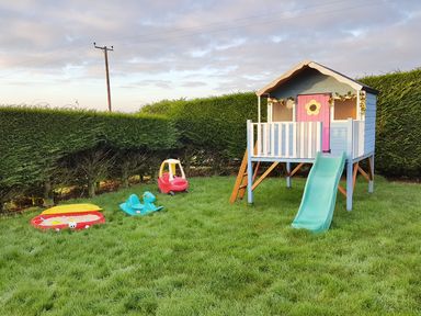 A backyard with a playhouse slide toy car rocking horse and sandbox at The Old Granary in Polyphant near Launceston