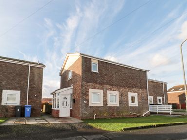 A two-story brick house with white framed windows and a white front door with a small front garden at Cheviot View in Beadnell