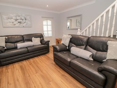 A living room with two black leather sofas wooden floor a side table a mirror a door and staircase at Cheviot View in Beadnell