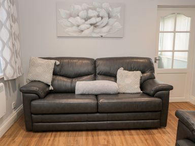 A dark leather sofa with three cushions and a painting of a flower on the wall behind at Cheviot View in Beadnell