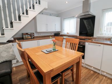 A kitchen with wooden dining table and chairs under a staircase with white cabinets and appliances at Cheviot View in Beadnell