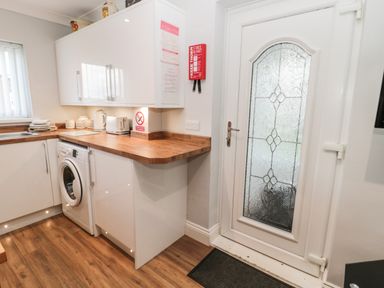A kitchen corner with white cabinets a washing machine wooden countertop and a glass panel door at Cheviot View in Beadnell